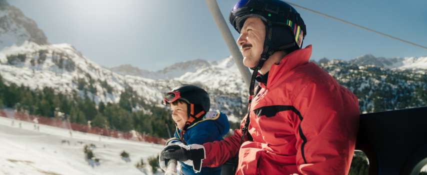 Dad and son who purchased travel insurance for skiing travelling on a chairlift
