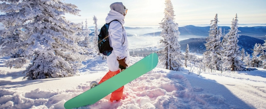 Woman holds snowboard against background of winter forest