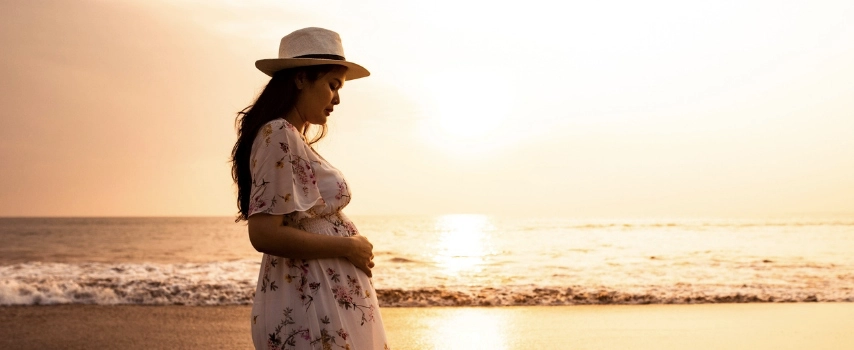 Pregnant female traveller standing on the beach 