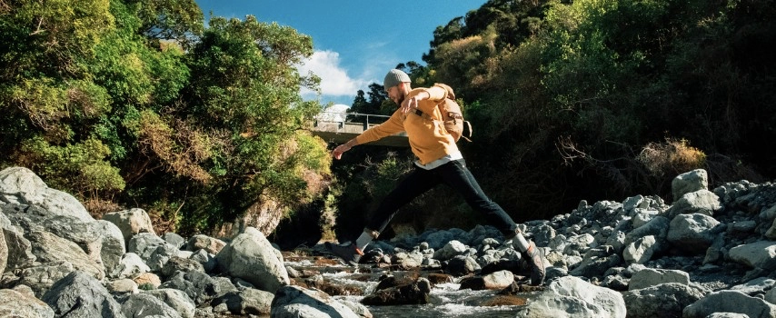 Man stepping across rocks in a river in New Zealand