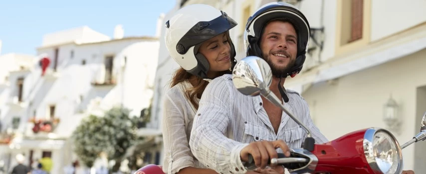 Young couple driving a moped through streets of Ibiza