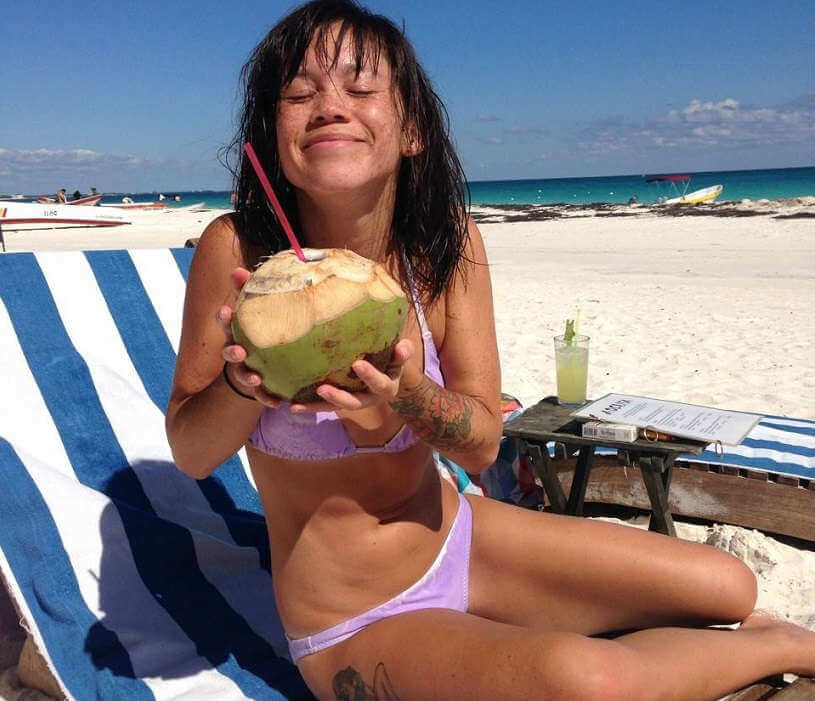 Emma Chow drinking a cocktail out of a coconut on Tulum beach, Mexico