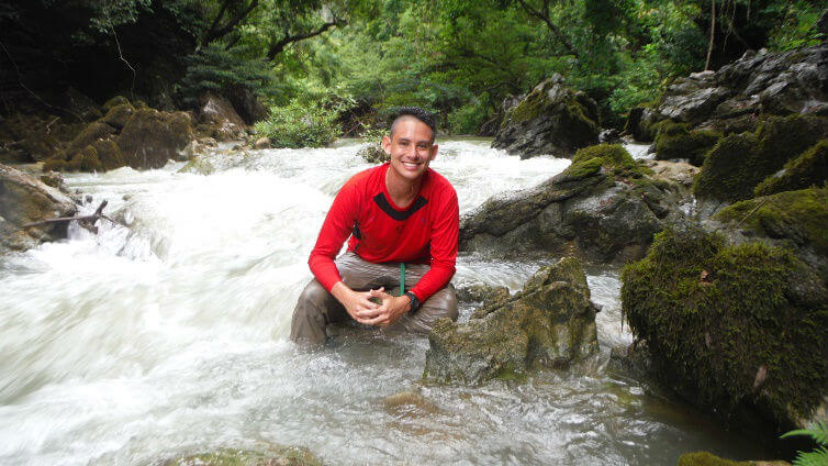 Photo of Samuel sitting in a flowing river at the Cave Kingdom of Vietnam